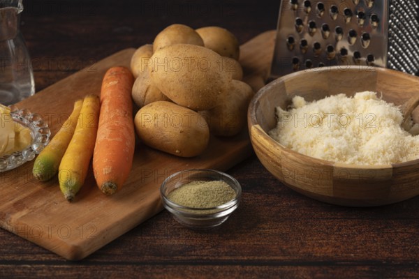 Potatoes, carrots and cheese on a table with spices and a grater