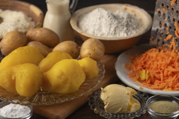 Boiled potatoes and grated carrots next to flour, milk and butter