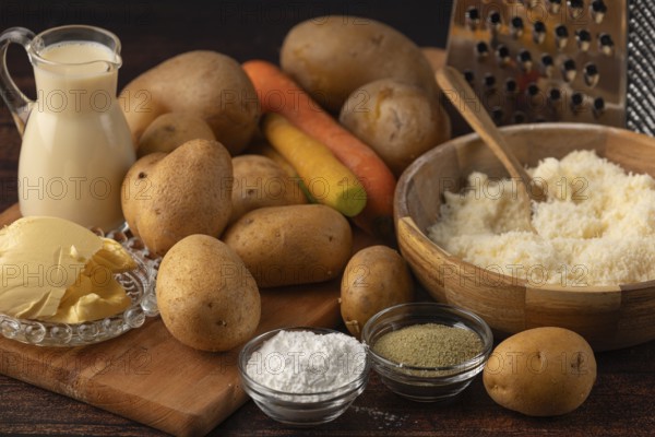 Kitchen ingredients with potatoes, carrots, parmesan and spices next to a grater