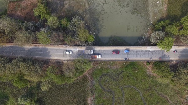 Aerial top-down view of vehicles traveling along a rural road bordered by wetlands and dense greenery