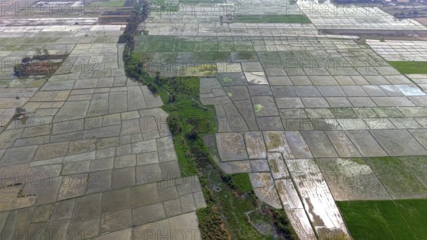 Aerial view of expansive agricultural fields divided into rectangular plots with a narrow green water channel running through the landscape