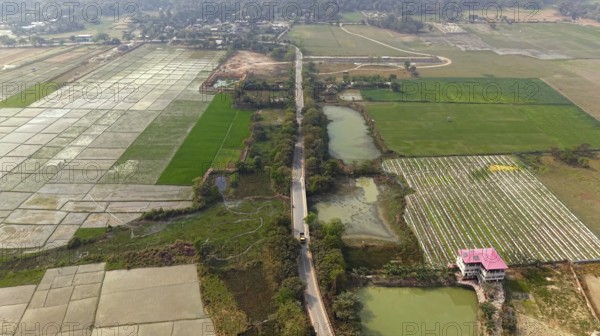 Aerial view of a rural road cutting through patchwork agricultural fields and ponds in the countryside