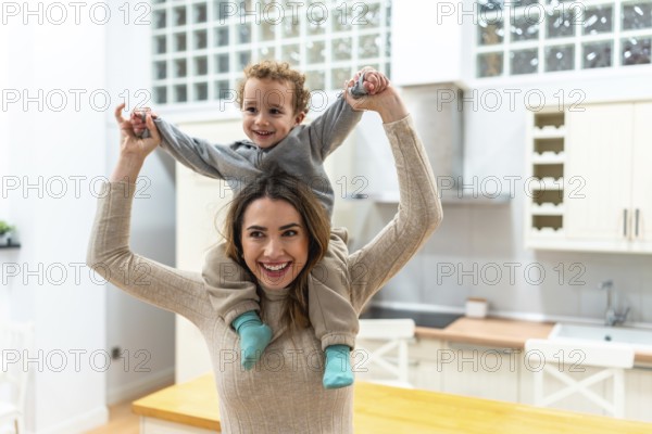 Happy mother giving her young son a piggyback ride, both smiling and interacting with joy and love in a bright home kitchen environment, showing family bonding and parenthood