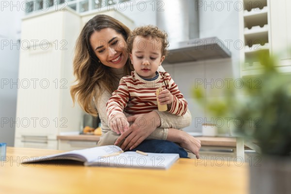 Loving mother embracing her happy young son while they are drawing together with colored pencils in a cozy modern home kitchen, sharing a tender moment of learning and bonding