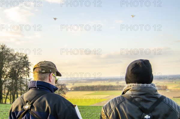Two people drone pilots Copter watch drones over a vast landscape at sunset, Lower Saxony, Germany