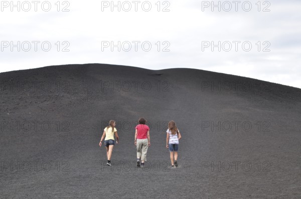 Three people hiking up a trail surrounded by gray lava rock, Craters of the Moon National Monument, Idaho, USA