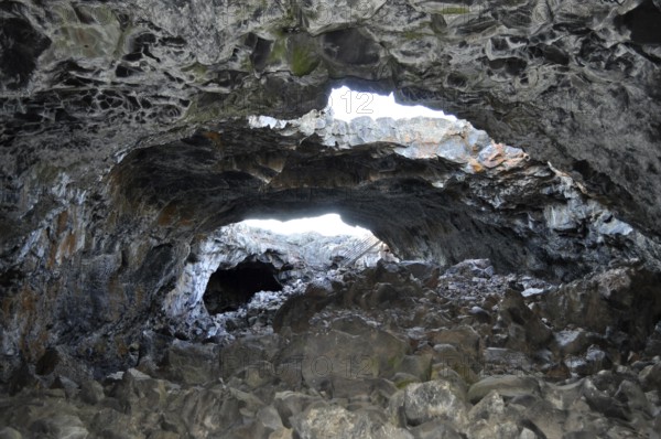 Rocky lava cave opening with irregular walls through which bright light shines in, Craters of the Moon National Monument, Idaho, USA