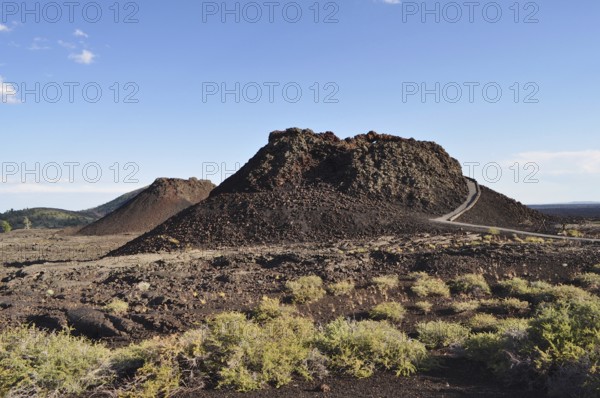 Volcanic cone with lava rock and sparse vegetation crossed by a hiking trail, Craters of the Moon National Monument, Idaho, USA