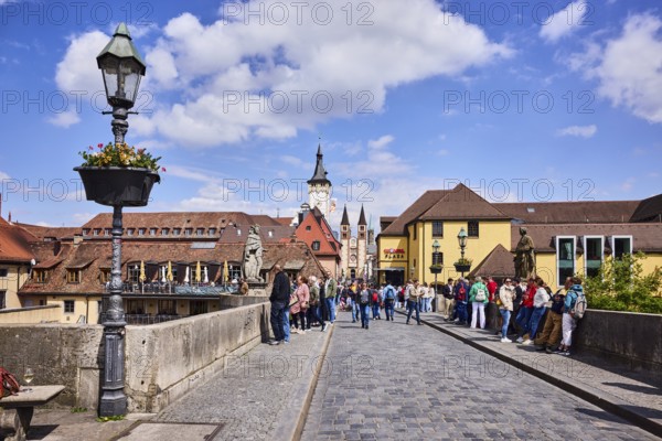Old Main bridge, footbridge, concrete wall, lantern, suspended flower pot, houses, bridge saint, town hall tower, double tower, cobblestones, paving stones, pedestrians as a secondary motif, blue sky, cumulus clouds, Würzburg, Lower Franconia, district-free city, Bavaria, Germany