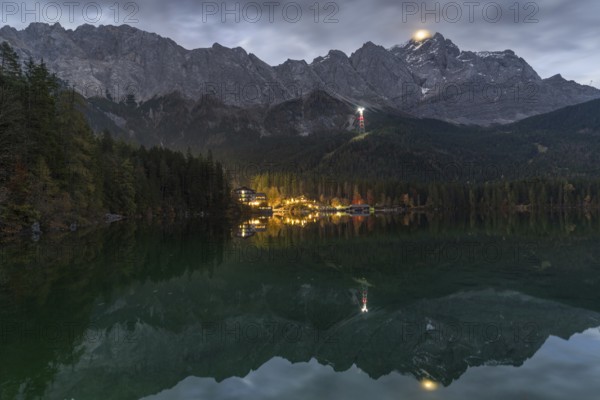 A stunning night view of Eibsee, surrounded by the Bavarian Alps The illuminated village reflects on the calm waters of the lake, creating a magical and tranquil alpine scene