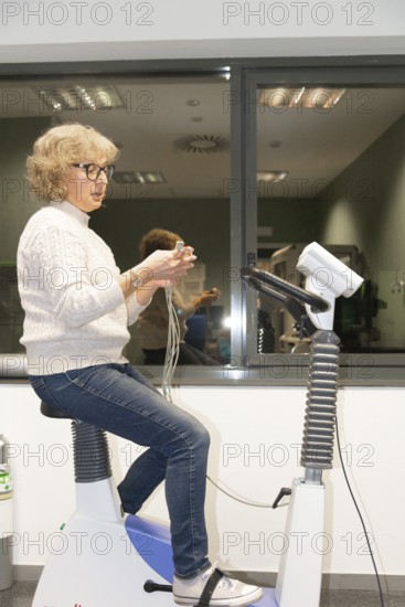 A mature woman performs a spirometry test to assess her lung function in a hospital setting, using a spirometer while seated