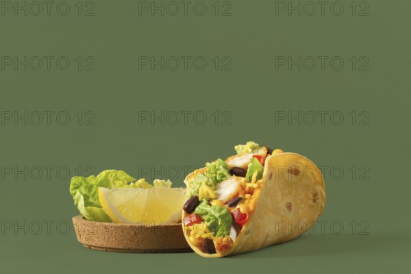 A vibrant taco filled with fresh vegetables, chicken, and cheese, complemented by slices of lemon and lettuce Set against a green background, showcasing a healthy meal