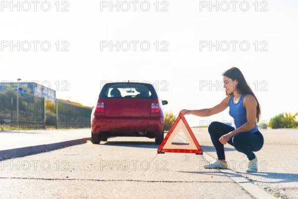 A young woman places a reflective warning triangle behind her car on a roadside This safety precaution is crucial for alerting other drivers during vehicle breakdowns