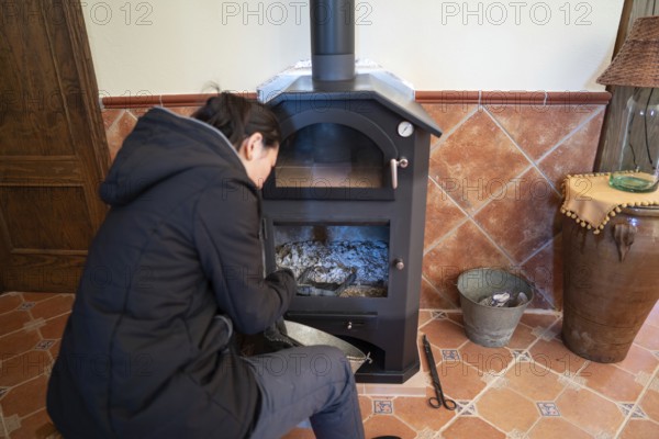 Back view of an Asian woman is cleaning the wood burning stove ashes, preparing it for use, paying attention only to her task