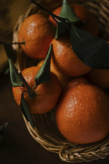 A close-up image capturing juicy oranges with vivid green leaves, nestled within a rustic woven basket. The oranges, glistening with freshness, embody vitality and natural beauty