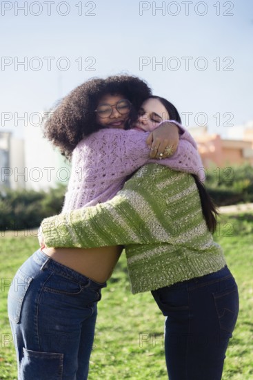 Two friends embracing joyfully in a sunny park, wearing cozy sweaters and jeans. Their happiness is evident, capturing a moment of warmth, friendship, and connection