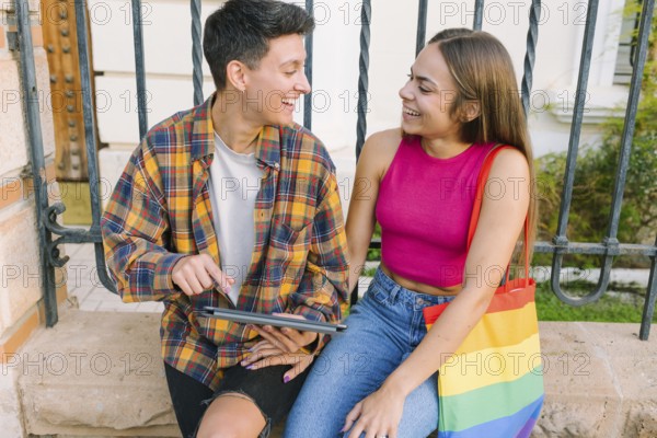 A joyful lesbian couple enjoys a happy moment outdoors, sharing smiles and warmth. They represent love, inclusivity, and LGBTQIA+ pride with a rainbow-colored accessory