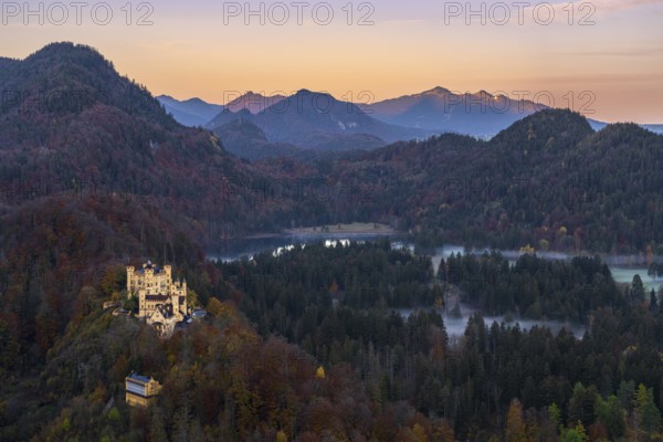 Scenic view of Hohenschwangau Castle amidst the vibrant autumn foliage of the Bavarian Alps The sunset casts a warm glow over the mountains and forested landscape