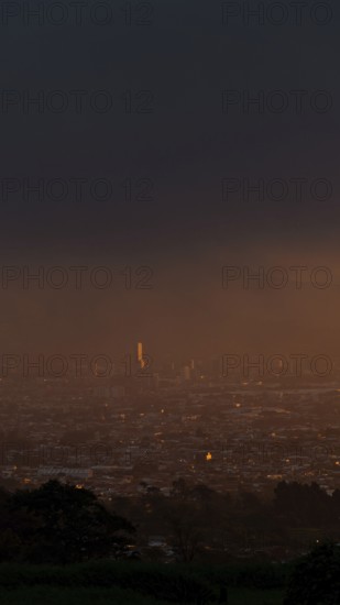 A serene sunset over San Jose, Costa Rica, captured from a mountain vantage point. The capital city bathes in a golden glow, evoking a peaceful urban evening