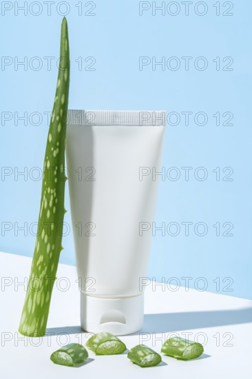 This image portrays a simple and clean representation of beauty and skincare featuring a white tube of aloe vera cream accompanied by a fresh aloe vera leaf and sliced pieces, staged against a soft light blue backdrop