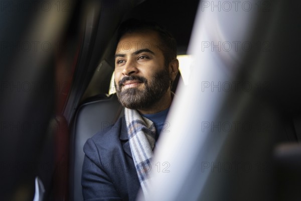 An Indian businessman in a cozy winter outfit looks contemplatively out of a car window, showcasing a serene and thoughtful expression