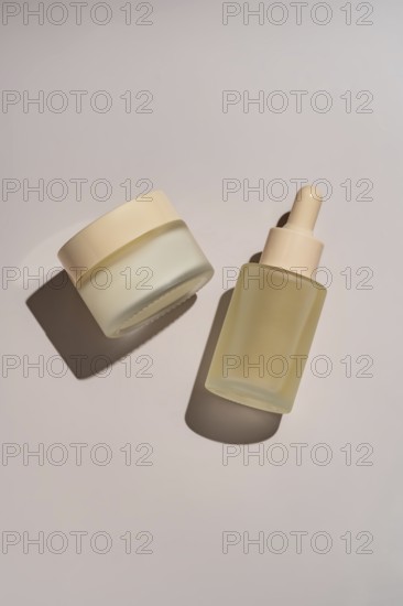 Skincare jar and dropper bottle with minimalistic design on a neutral background The glass containers cast soft shadows, emphasizing elegance and simplicity in beauty products