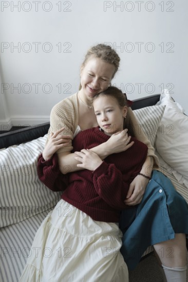 A tender moment of a mother and daughter sharing an embrace while seated on a cozy couch, capturing the warmth and affection of their bond in a serene, homey setting