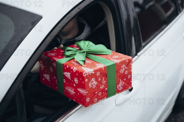 A person hands a festive gift wrapped in red with a green bow from a car window The scene captures a moment of giving, highlighting joy and holiday spirit