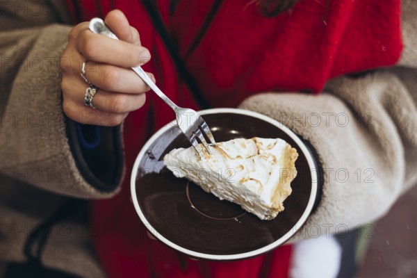 Cropped unrecognizable woman outside wearing winter garments, focusing on her hands as she uses a fork to take a bite of pie from a plate