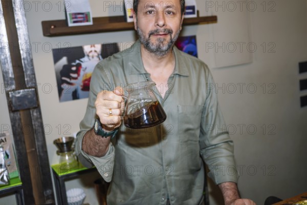 A barista in a cozy cafe confidently showcases a pot of freshly prepared specialty coffee