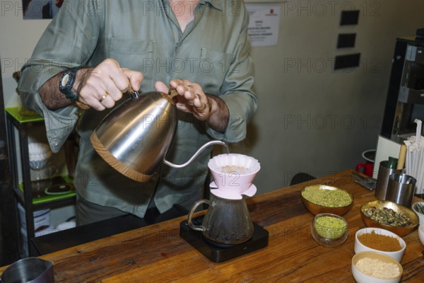 A barista carefully pours hot water into a dripper, crafting specialty coffee with precision. Surrounded by bowls of ingredients, the table showcases the art of coffee making