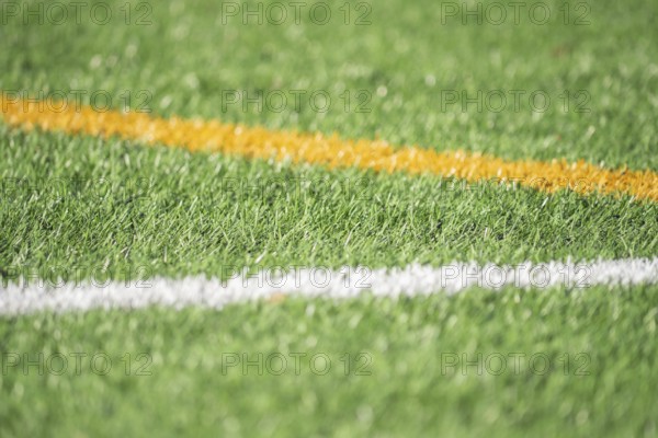 A detailed close-up of green artificial turf with bold white and yellow lines, capturing the texture and vibrant contrast often seen on soccer fields