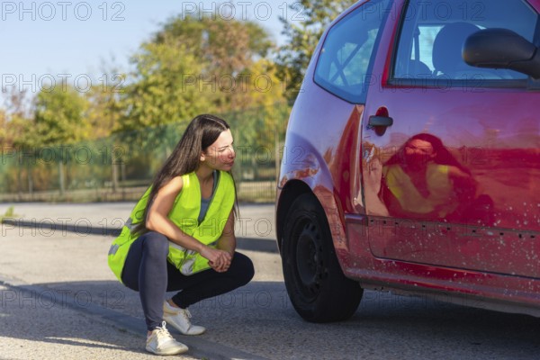 A woman in a high-visibility vest examines the damage on a red car after a minor accident The scene captures concern and attention to detail in dealing with vehicle incidents