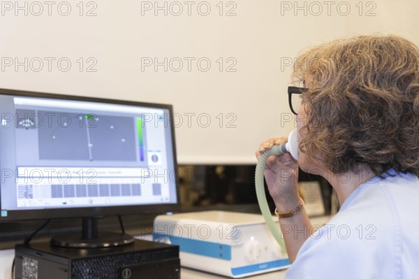 A middle-aged woman undergoing a spirometry test in a pneumology department, displaying her breath capacity on a computer monitor