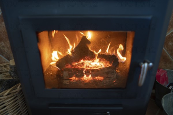 A wood burning stove with bright flames consuming logs, showcasing the warmth and rustic charm of indoor heating. The fiery orange hues illuminate the stove interior, enhancing the cozy atmosphere