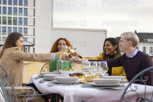 A joyful group of friends toasting with wine glasses on a rooftop The table is elegantly set, capturing a lively celebration with smiles and cheerful conversations