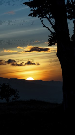 Captivating scene of the sun setting behind the silhouetted mountains, viewed from a vantage point overlooking San Jose, Costa Rica. The sky is painted in vibrant shades of orange and blue, with scattered clouds illuminated by the sunset