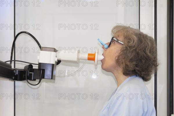 A woman is shown with nose clip performing a spirometry test to assess her lung function in a clinical setting within a pneumology department. Essential medical evaluation highlighted