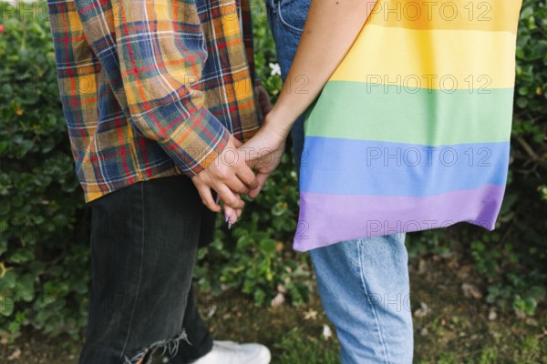 A touching close-up of a lesbian couple holding hands, symbolizing love and unity. One partner carries a bag with the Pride flag, representing LGBTQIA+ pride, inclusivity, and diversity