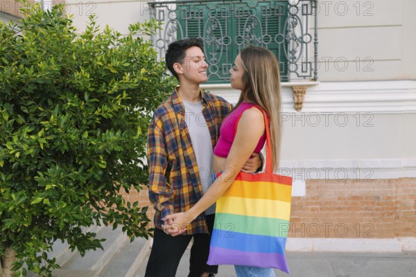 A loving lesbian couple shares a warm embrace while holding hands in an urban setting. One partner carries a Pride flag bag, symbolizing LGBTQIA+ pride, inclusivity, love, and diversity