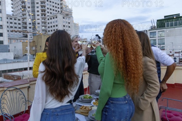 A lively group of friends celebrates on a rooftop, raising glasses in a toast Surrounded by city buildings and festive string lights, they enjoy a joyful party atmosphere