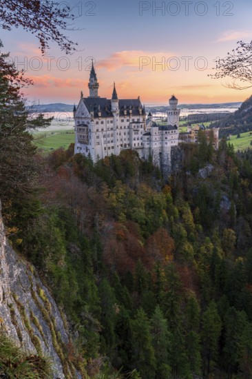 Neuschwanstein Castle stands majestically amidst a vibrant autumn forest in the Bavarian Alps Sunset enhances the scene with warm hues, highlighting this iconic landmark