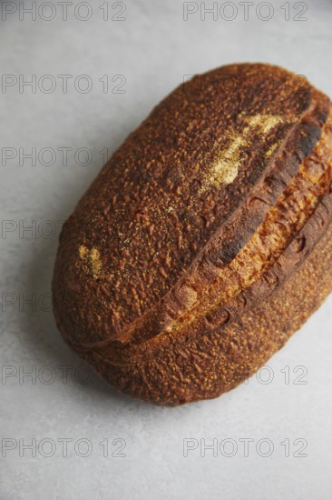 Top view of a freshly baked sourdough bread loaf with a dark, crispy crust on a textured background