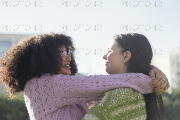 Two friends share a warm embrace in a sunlit park, wearing cozy sweaters. Smiling and enjoying each other company, they express joy and friendship in the crisp outdoor air