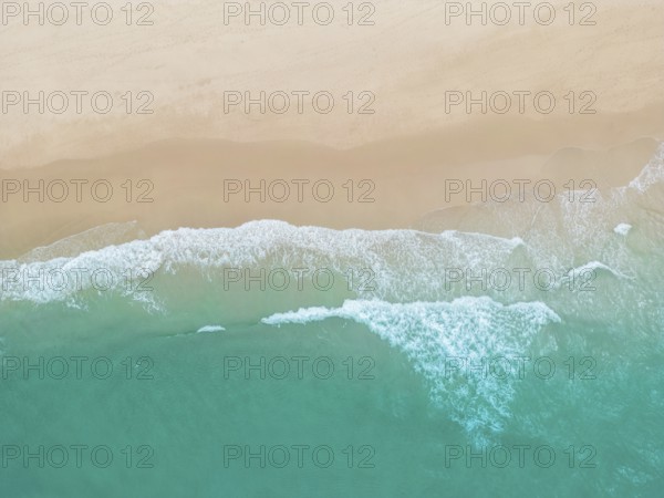 A breathtaking aerial photograph of a sandy beach in Portugal, where gentle turquoise waves meet the shore. Captures the natural beauty and tranquility of the Portuguese coastline