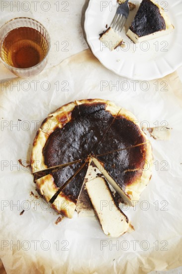 Top view of a minimalist photograph showcasing a freshly baked San Sebastian cheesecake, served on parchment paper with a honey glass aside