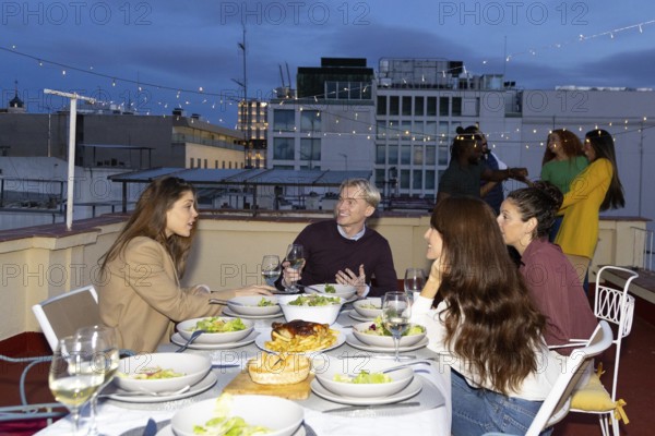 A lively group of friends enjoys a rooftop dinner party The scene captures a festive atmosphere with laughter, gourmet dishes, and sparkling string lights during the evening