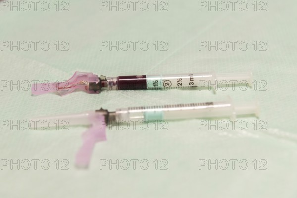 A close-up image of medical syringes filled with blood, laid on a sterile aqua-colored surface, typically used for blood tests in clinical settings