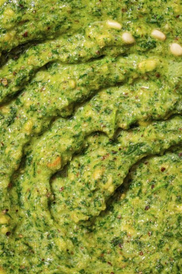 Top view close-up of freshly made pesto sauce showcasing its vibrant green color and texture speckled with pine nuts, garlic, and assorted herbs