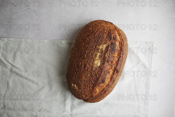 Top view of a freshly baked sourdough bread with a crispy crust, resting on a white linen cloth, offering a perfect example of traditional home baking
